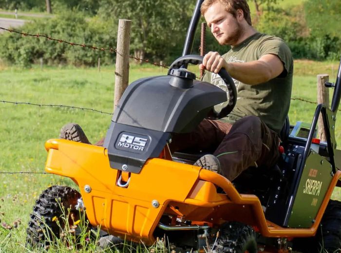 Ein Mann fährt auf einem orangefarbenen AS Motor Wiesenmäher über eine grüne Wiese.