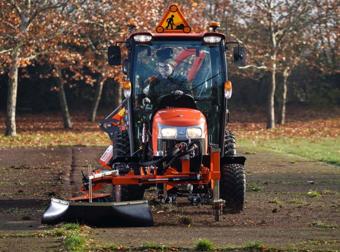 Ein Traktor steht auf einer gepflasterten Straße, neben der Ecotech Wildkrautbürste WKT-7