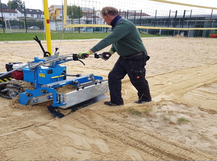 Ein Mann bedient eine Fiorentini Sandreinigungsmaschine, um einen Volleyballfeld am Strand zu säubern