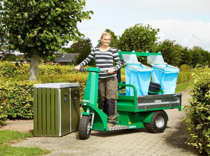 Eine Frau fährt auf einem Scooter neben einem Mülleimer, GMR Maskiner Stama Micro EL im Hintergrund sichtbar