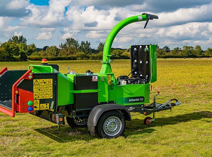 Eine grüne Greenmech Arborist 150 Maschine steht in einem Feld, umgeben von frischem Gras und Pflanzen