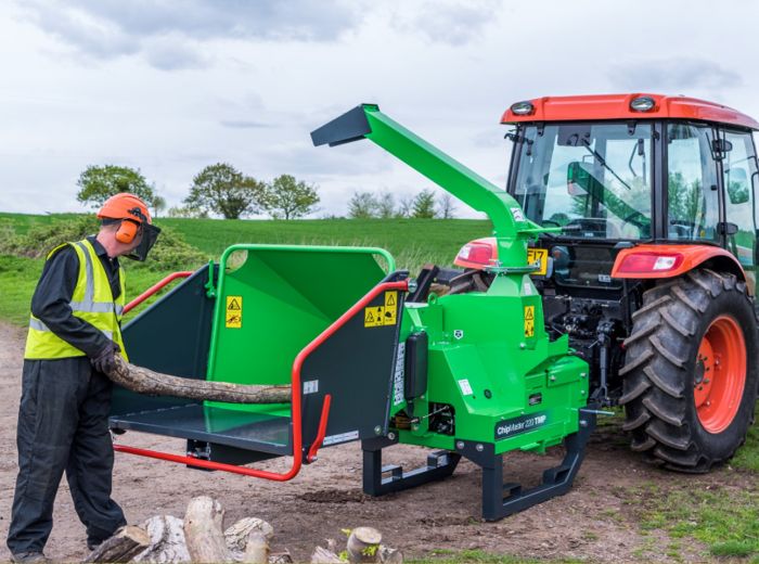 Ein Mann fährt mit einem grünen Greenmech Chipamster 220TMP Traktor, um ein großes Holzstück zu bewegen