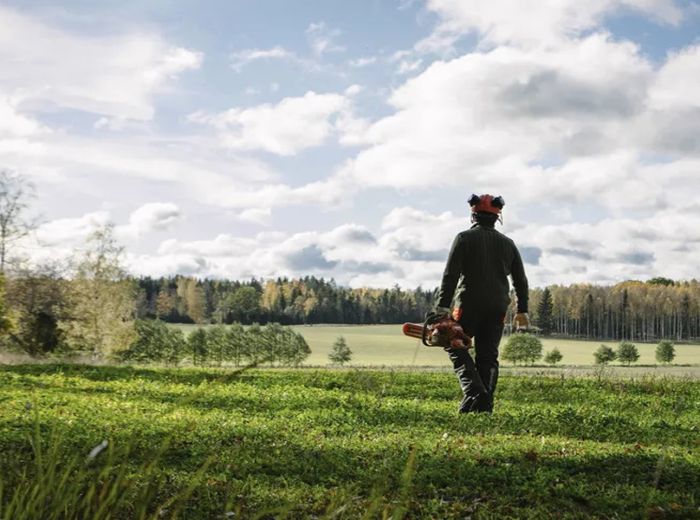 Ein Mann in einem Feld mit Rucksack, der eine Husqvarna Kettensäge in der Natur präsentiert