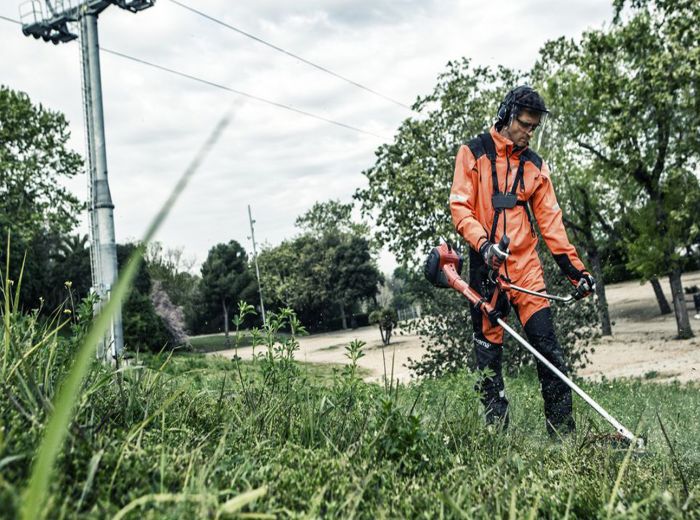 Mann in orangefarbener Jacke nutzt einen Husqvarna Freischneider zum Rasenmähen