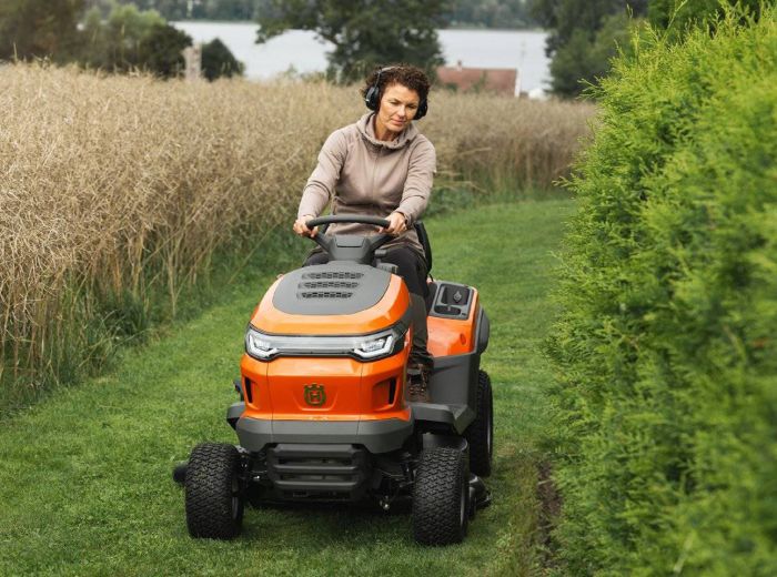 Frau auf einem orangefarbenen Husqvarna Rasentraktor, der über eine grüne Wiese fährt