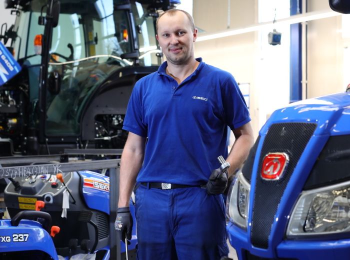 Ein Mann in einer Iseki-Werkstatt steht neben einem Traktor, der für Reparaturen vorbereitet ist
