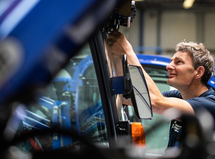 Ein Mann repariert ein blaues Fahrzeug in der Iseki Werkstatt, umgeben von industrieller Ausstattung und Werkzeugen