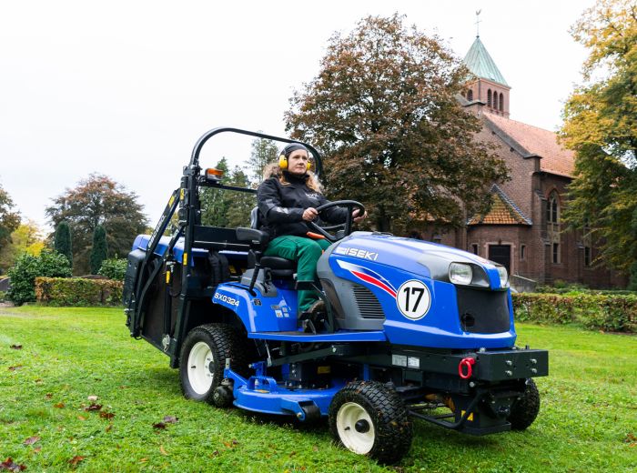Ein Mann lenkt einen blauen Traktor vom Typ Iseki sxg324 auf einem grasbewachsenen Feld