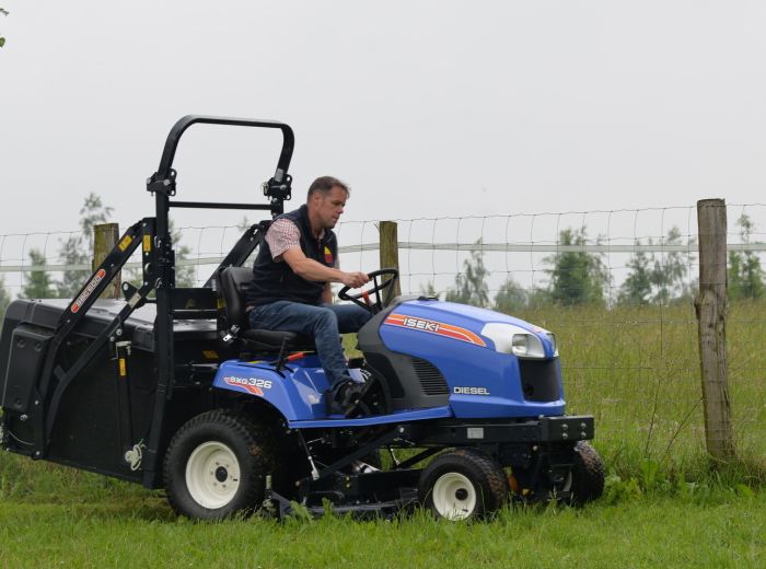 Ein Mann steuert einen blauen Iseki Traktor SXG326 durch ein offenes Feld