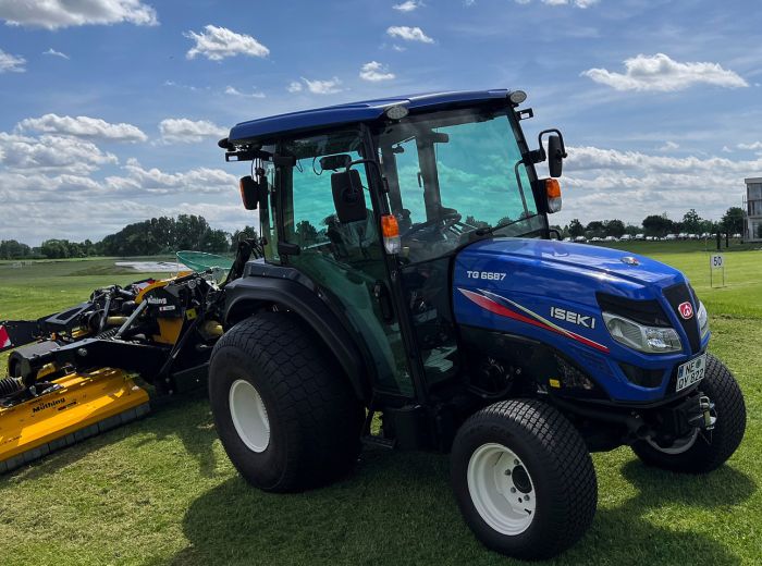 Iseki TG6687 Traktor in Blau, geparkt auf dem Rasen mit Golfplatz im Hintergrund