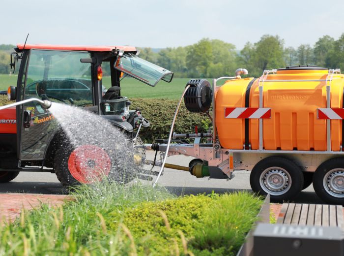 Ein Traktor sprüht Wasser auf einen Bewässerungsanhänger von Jansing & Hidding.