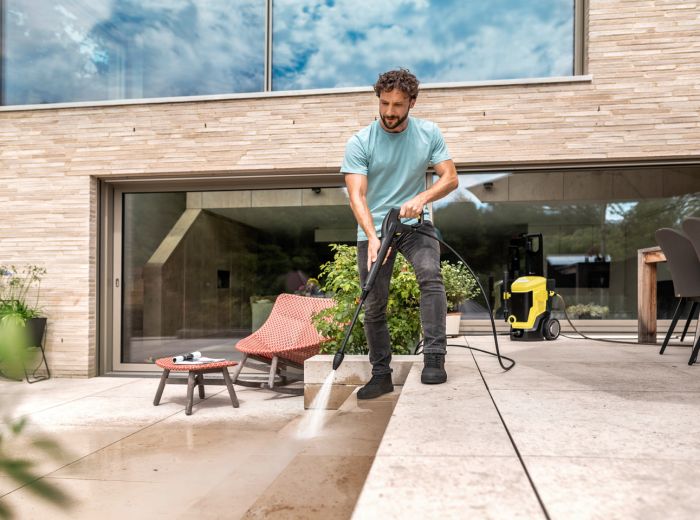 Ein Mann reinigt mit einem Hochdruckreiniger eine Terrasse im Freien. Kärcher Reinigung für die Außenterrasse