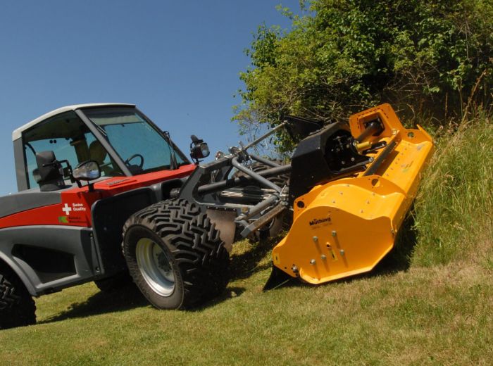Ein Kalinke Aebi Terratrac-Traktor mit großer gelber Schneide auf einer grünen Wiese