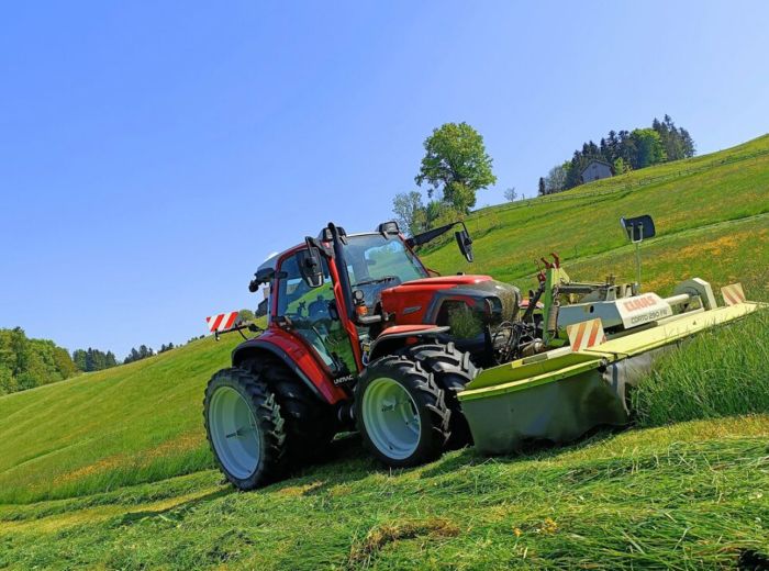 Lindner Traktor mäht Gras auf Hang in grüner Landschaft