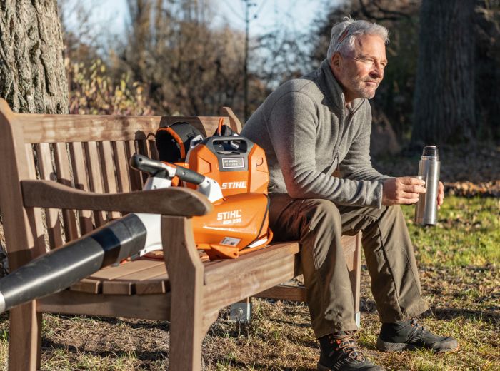 Ein Mann sitzt auf einer Bank mit einem Rucksack und einem Laubbläser von Stihl BGA 200 neben sich