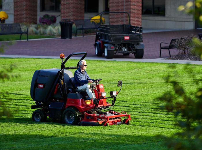 Ein Mann fährt auf einem roten Rasenmäher der Marke Toro PLH 800
