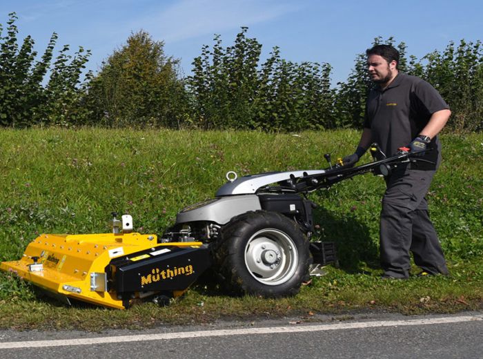 Ein Mann mäht mit einer kleinen gelben Maschine eine Rasenfläche. Muething Mu B