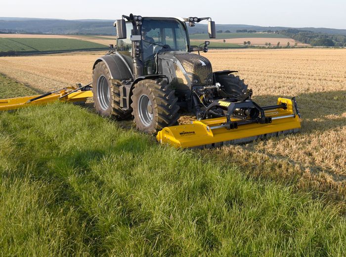Ein Traktor, ausgestattet mit Muething-Mulcher Vario, bearbeitet das Gras in einem Feld