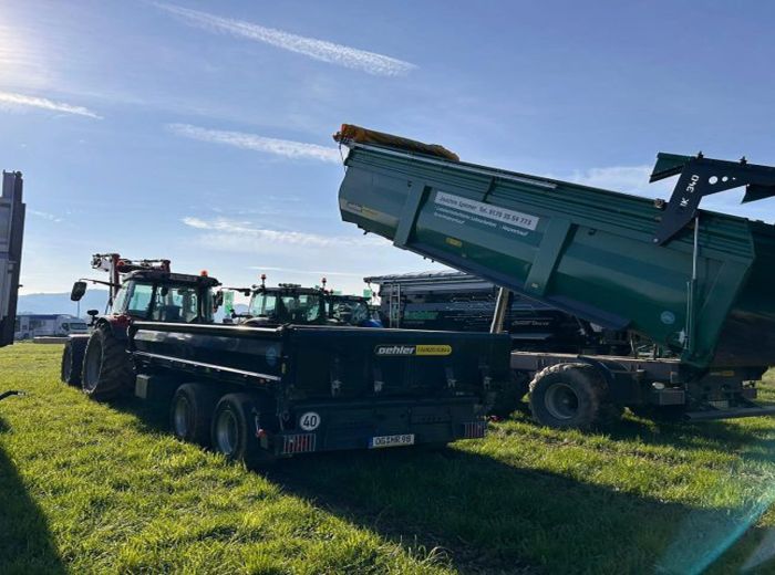 Ein grüner Kipper ist auf einem Feld abgestellt, mit dem Oehler Jubiläumsmesse Anhänger im Hintergrund