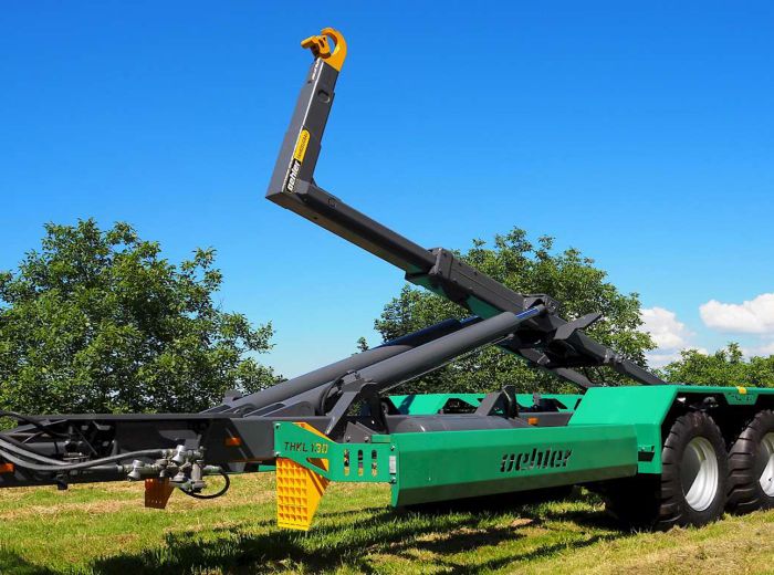 Grüner Traktor mit Kran, ausgestattet mit einem Oehler THKl130 Anhänger, auf einem Feld im Einsatz