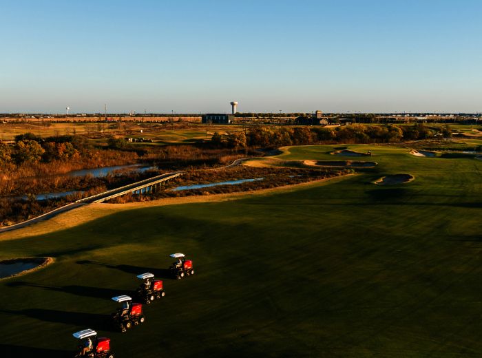 Golfplatz in PGA Frisco mit mehreren Golfcarts, umgeben von gepflegten Fairways und grünen Landschaften