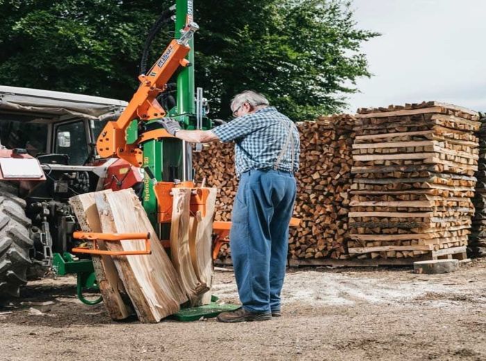 Mann neben einem Traktor und Holzstapel, inspiziert den Posch Hydrocombi Holzspalter im Freien