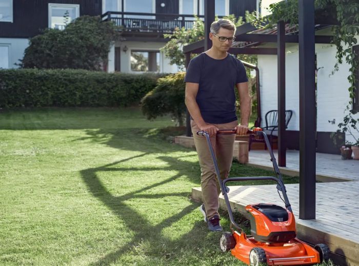 Ein Mann mäht den Rasen mit einem orangefarbenen Rasenmäher im Garten