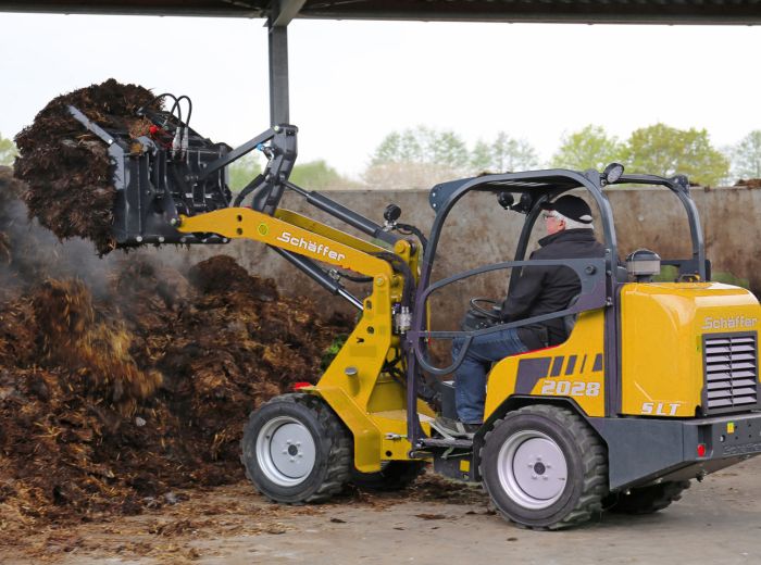 Ein Mann fährt einen gelb-schwarzen Schäffer 2028 SLT Lader auf einer Baustelle