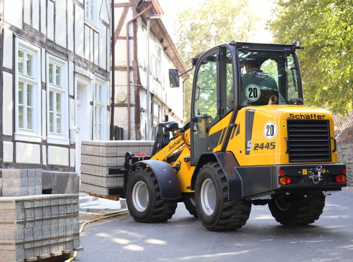 Gelbes und schwarzes Baufahrzeug, Schäffer 2445 s, fährt eine Straße entlang