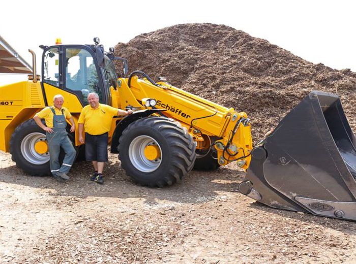 Zwei Männer stehen neben dem großen gelben Schäffer 9660T Radlader, der für Bauarbeiten eingesetzt wird