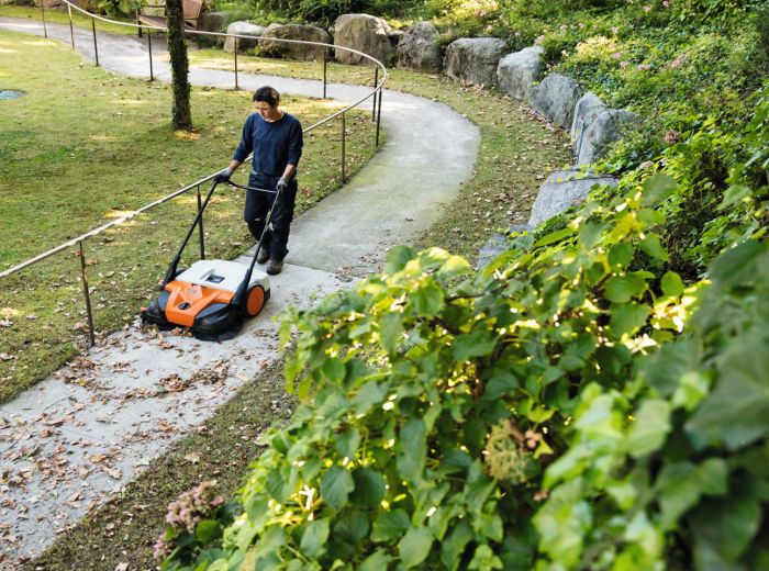 Ein Mann mäht mit einem Stihl Rasenmäher einen Weg in einem gepflegten Garten