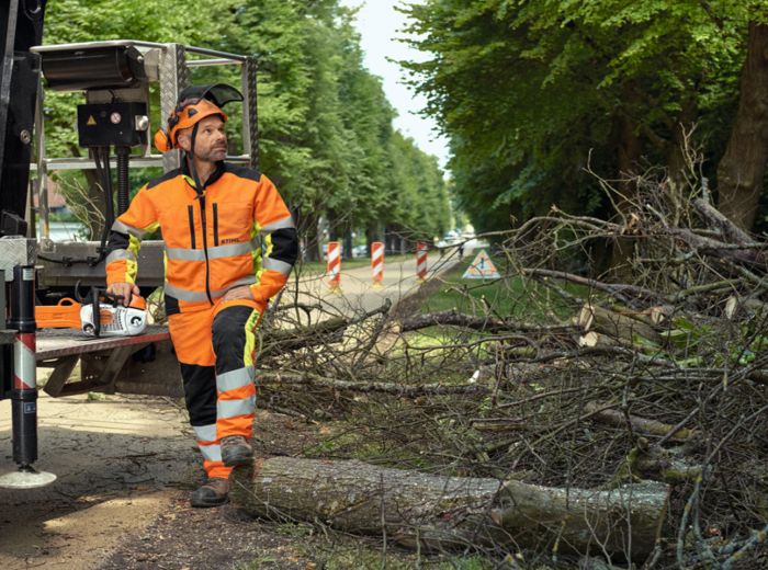 Ein Mann im orangefarbenen Sicherheitsanzug steht neben einem Stihl Protect MS Lkw