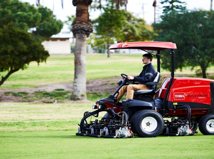 Ein Mann fährt einen roten Golfwagen, Toro Reelmaster 5510 d, über ein grünes Feld