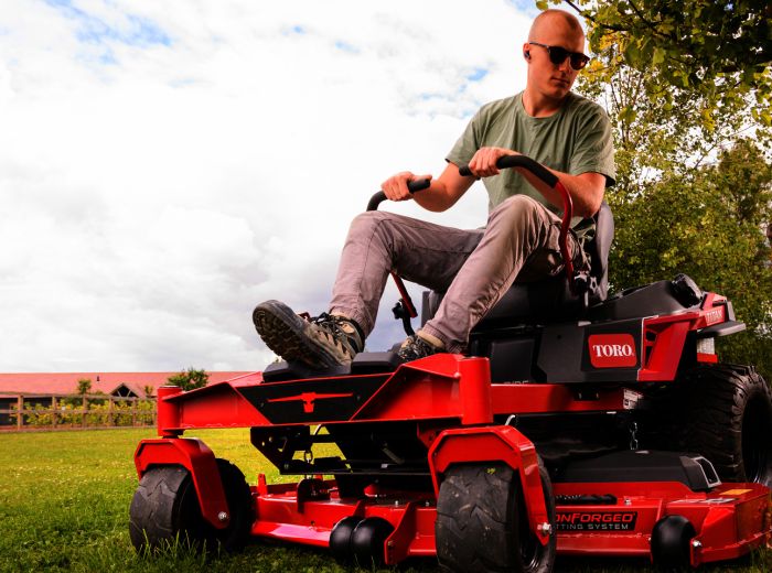 Ein Mann fährt auf einem roten Rasenmäher, dem Toro Titan ZXM6075, über eine grüne Wiese
