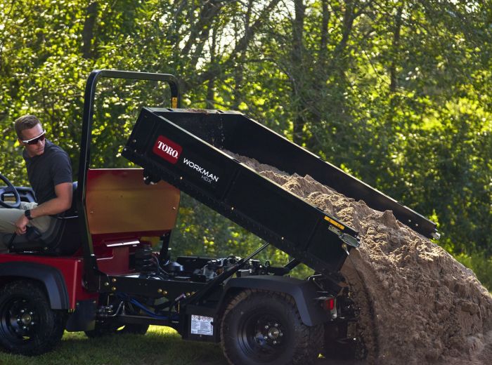 Ein Mann lädt Erde auf ein rotes Nutzfahrzeug, den Toro Workman HDX, für Transportarbeiten