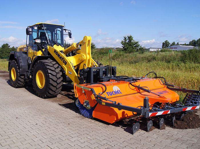Ein Traktor mit einem großen orangefarbenen Behälter steht am Straßenrand