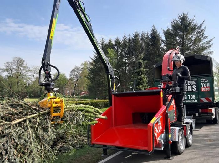Ein Mann lädt einen Baum auf einen Truck, während ein Ufkes Cheetah 30 Häcksler im Hintergrund steht.