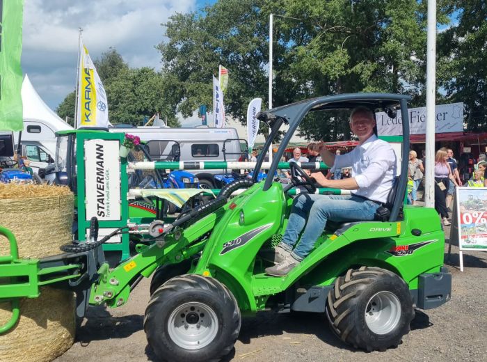 Ein Mann fährt einen grünen Traktor, beladen mit Heuballen, durch eine ländliche Umgebung
